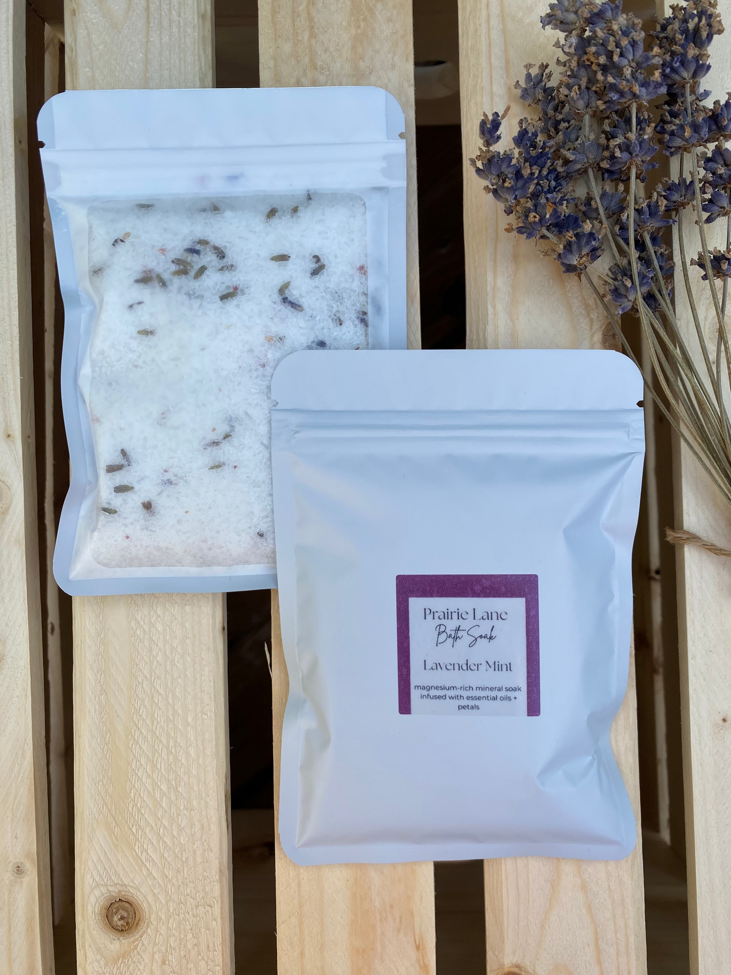 Packages of lavender bath salts on a wooden surface with dried lavender flowers.