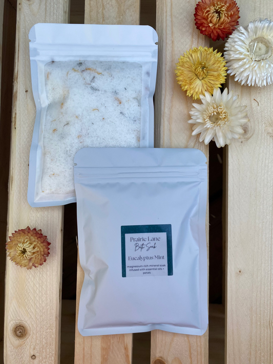 Package of bath salts with a labeled packet on a wooden surface with flowers.