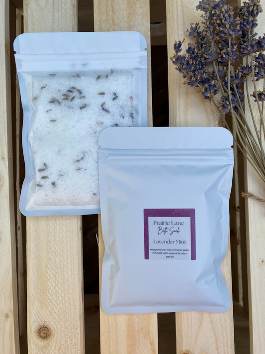 Packages of lavender bath salts on a wooden surface with dried lavender flowers.